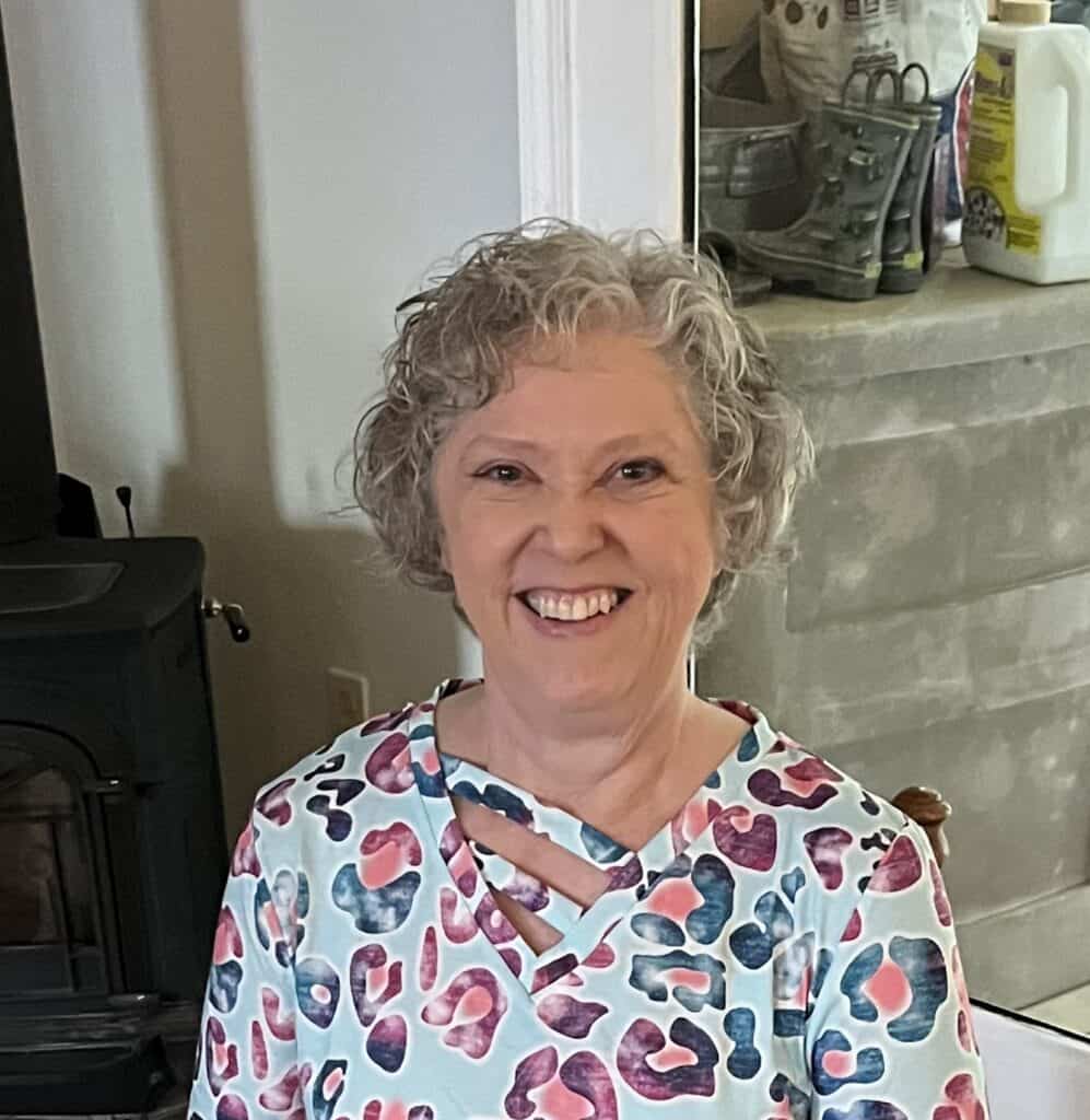 Smiling woman with curly gray hair sitting at a table, representing the board at Riverside Coffee Sh.