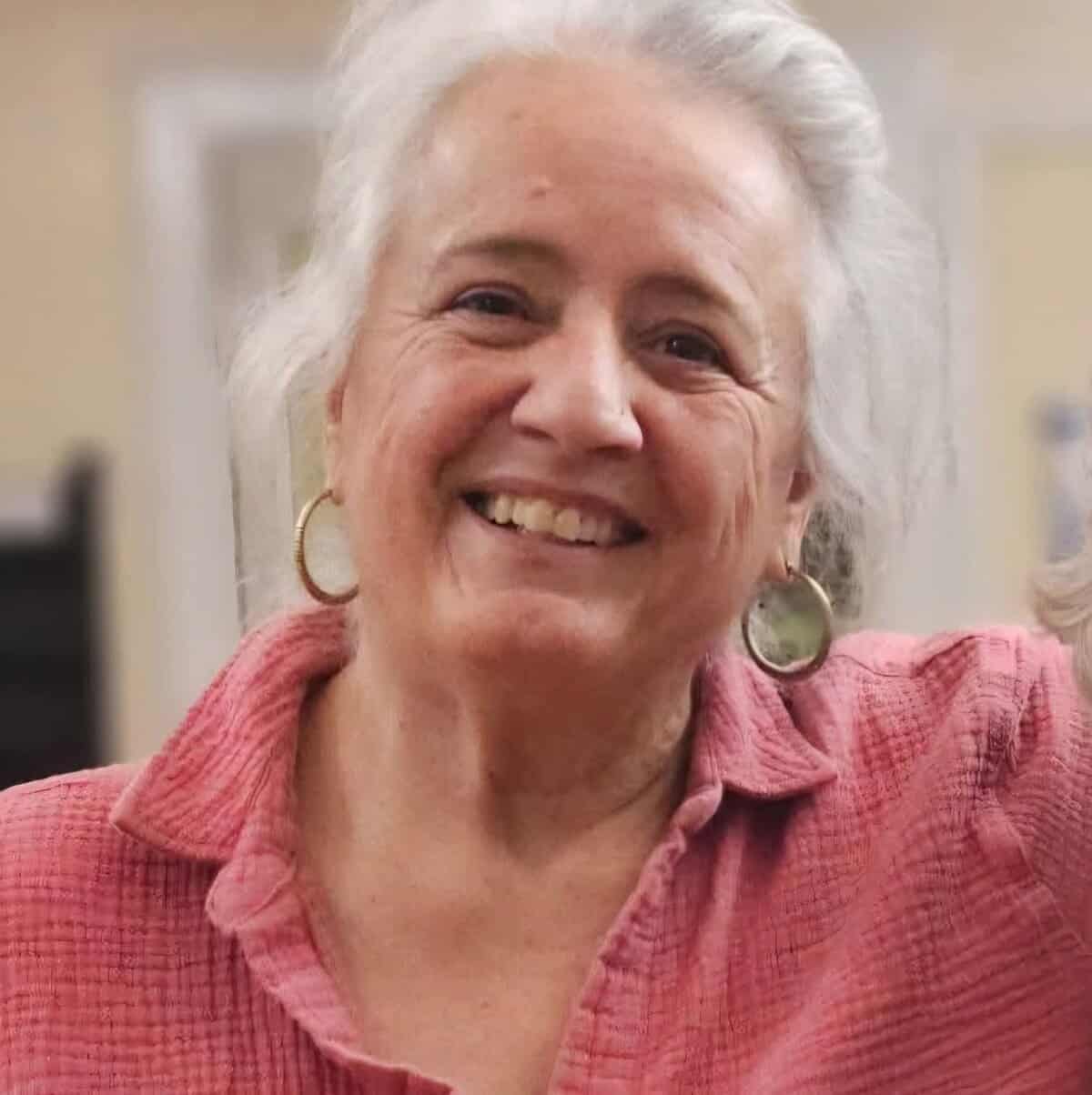 Smiling woman with white hair and pink shirt at Riverside Coffee Shop.